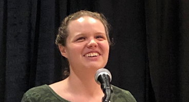 A member smiles as she speaks from a podium